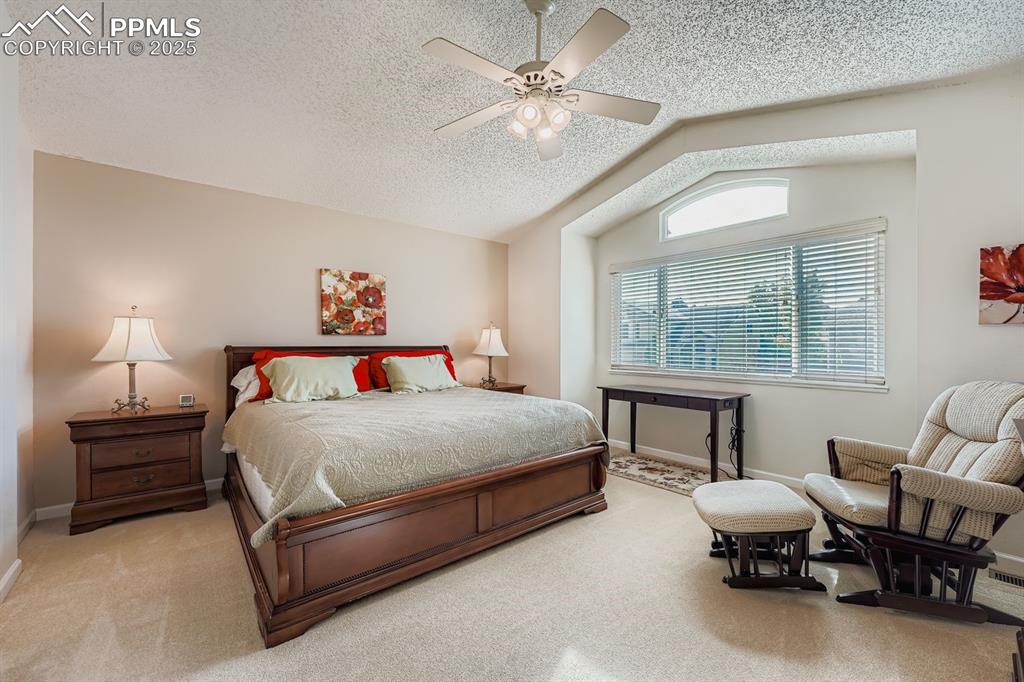 Bedroom featuring vaulted ceiling, carpet, ceiling fan, and a textured ceiling