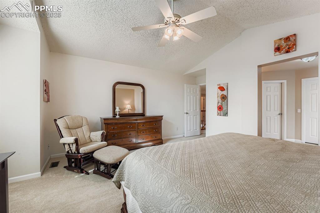 Bedroom with light carpet, vaulted ceiling, a textured ceiling, and a ceiling fan