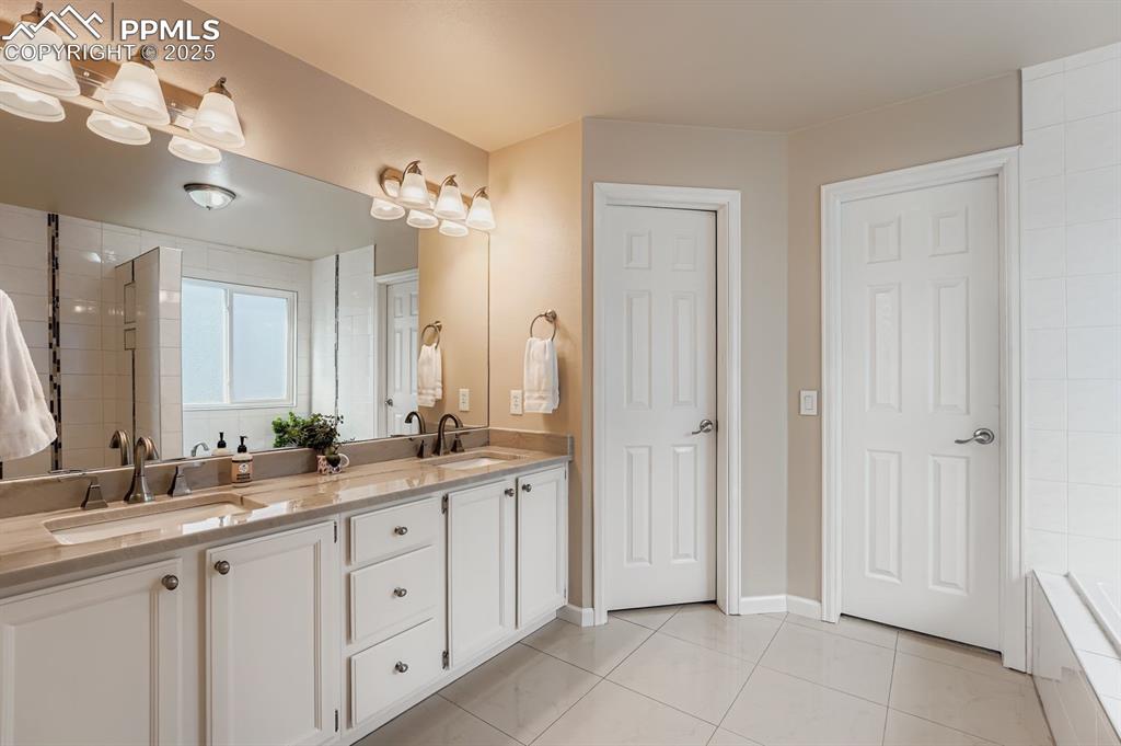 Bathroom with double vanity, light tile patterned floors, tiled shower, and a bath