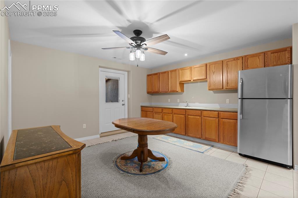 Kitchen featuring freestanding refrigerator, light tile patterned floors, a ceiling fan, and brown cabinets
