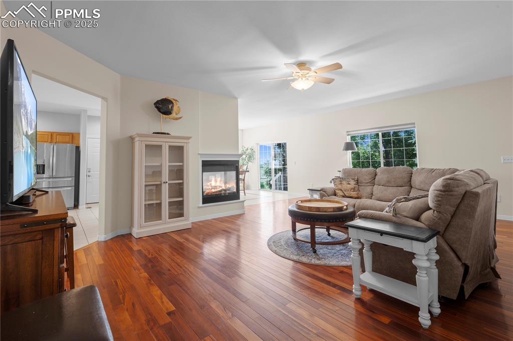 Living room with a ceiling fan, wood-type flooring, and a multi sided fireplace