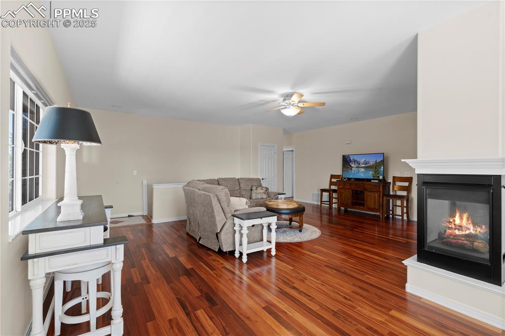 Living area featuring dark wood finished floors, ceiling fan, and a multi sided fireplace