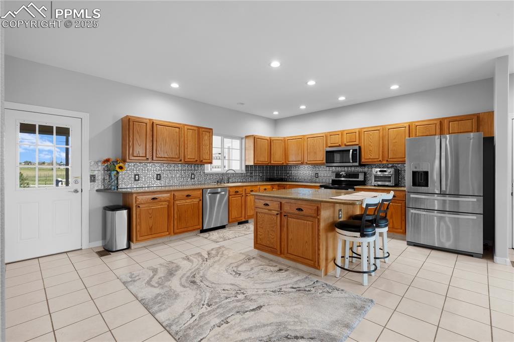 Kitchen featuring stainless steel appliances, backsplash, recessed lighting, a kitchen island, and light tile patterned floors