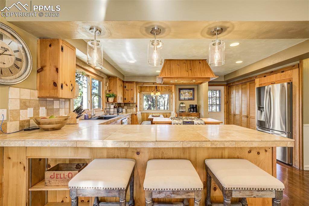 Kitchen featuring stainless steel fridge with ice dispenser, tile counters, a peninsula, backsplash, and dark wood finished floors