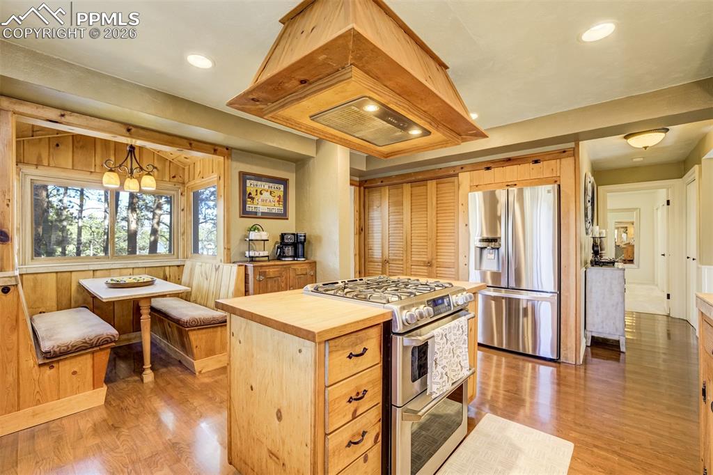 Kitchen with stainless steel appliances, gas range and island range hood, butcher block countertop island, eat-in banquette, and large pantry closet. 