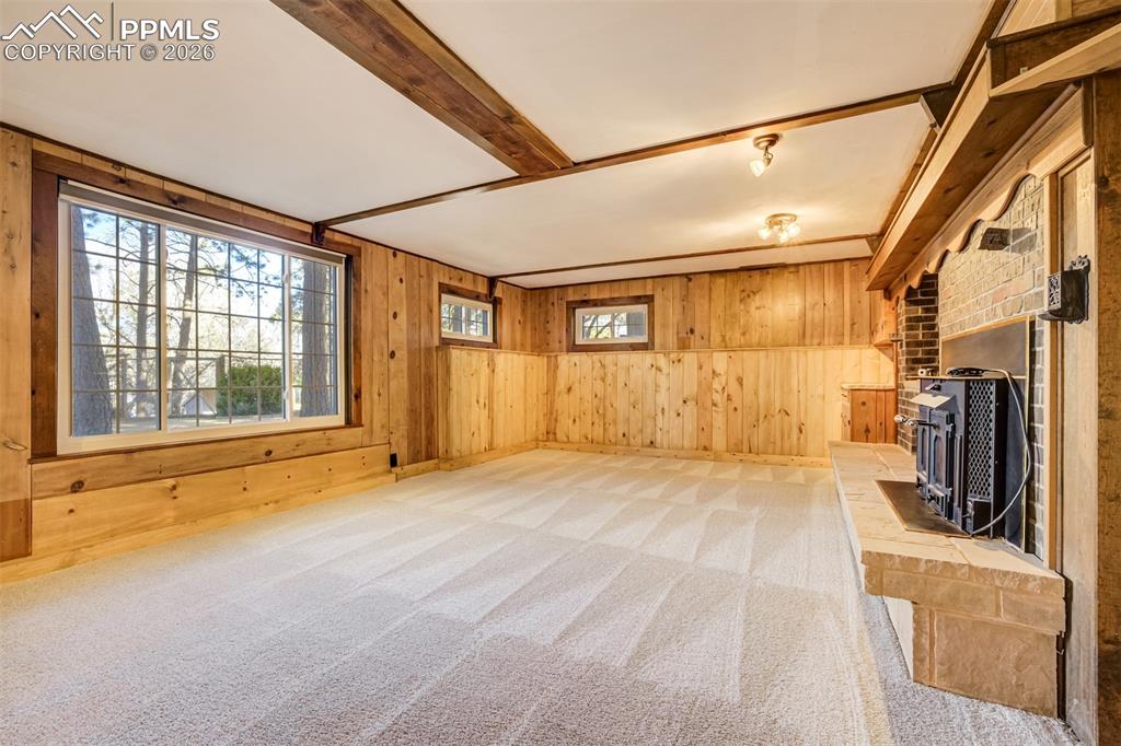 Family room featuring walkout, new carpet, wood walls, a brick wood burning fireplace, and beamed ceiling