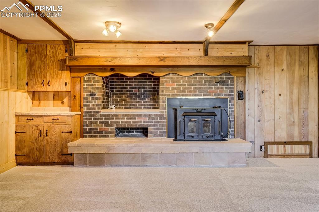Family room featuring walkout, new carpet, wood walls, a brick wood burning fireplace, and beamed ceiling