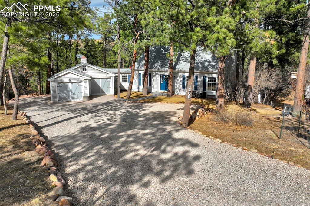 View of front of house with driveway and view of wooded area