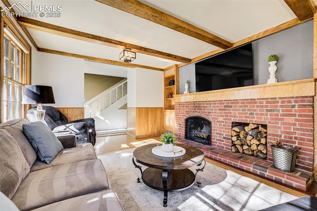 Main level living area with wood wainscoted wall, built in features, a fireplace, and beamed ceiling