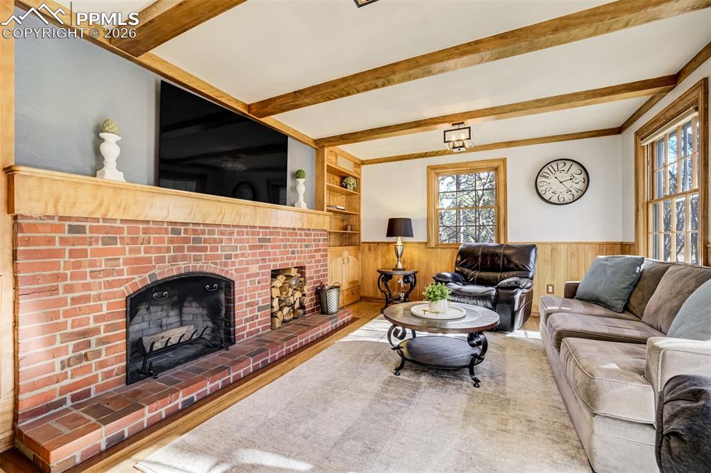 Main level living area with wood wainscoted wall, built in features, a fireplace, and beamed ceiling