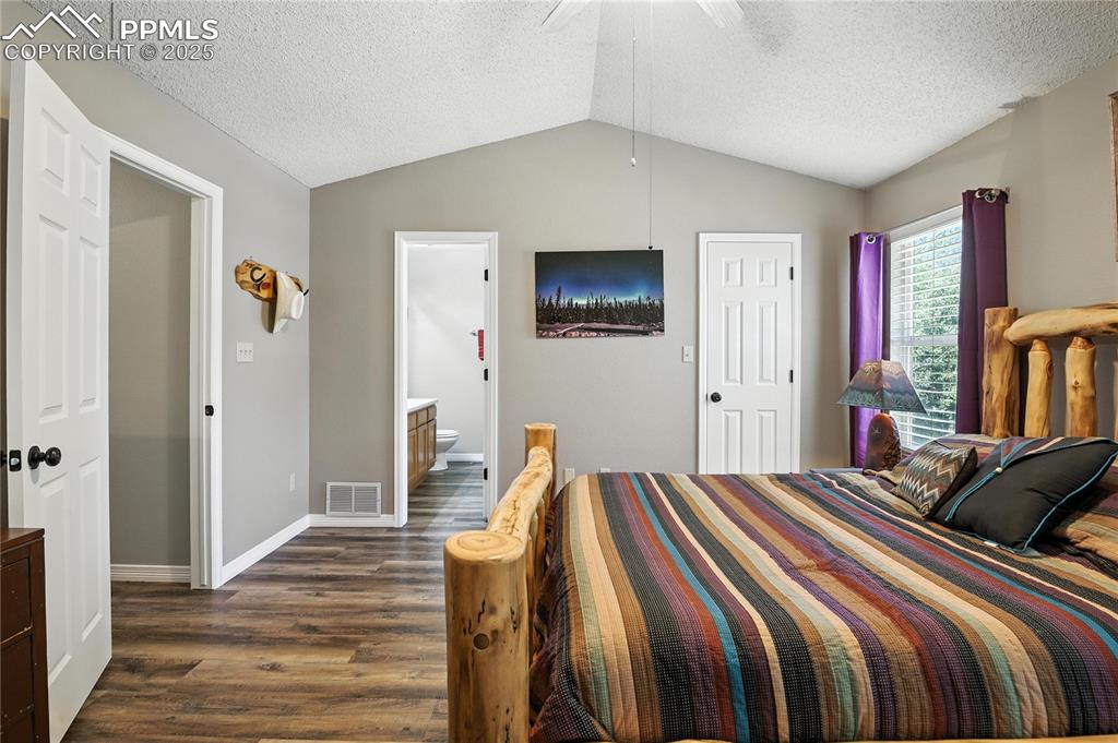 Bedroom with dark wood finished floors, lofted ceiling, a textured ceiling, connected bathroom, and ceiling fan