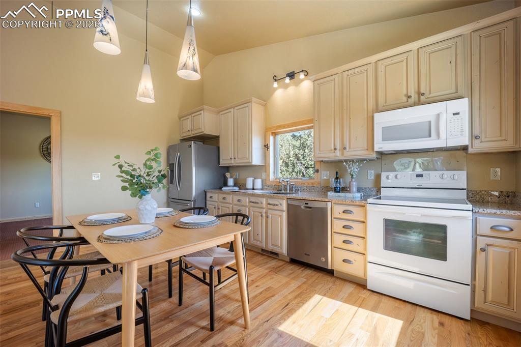 Kitchen with stainless steel appliances, lofted ceiling, light stone countertops, hanging light fixtures, and light wood-style flooring
