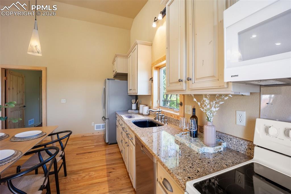 Kitchen with stainless steel appliances, light stone countertops, light wood-style floors, and hanging light fixtures