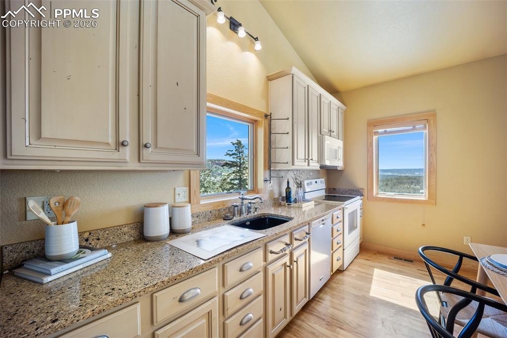Kitchen with white appliances, light stone countertops, light wood-type flooring, and cream cabinets