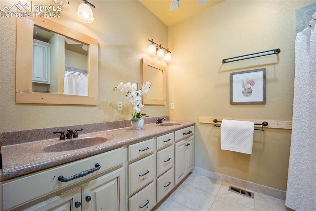 Bathroom with double vanity, a shower with curtain, light tile patterned flooring, a ceiling fan, and a textured wall