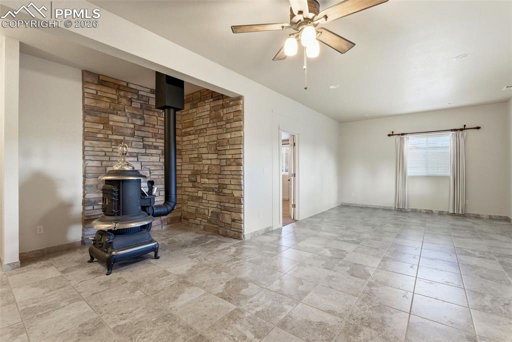 Unfurnished living room featuring a wood stove and ceiling fan