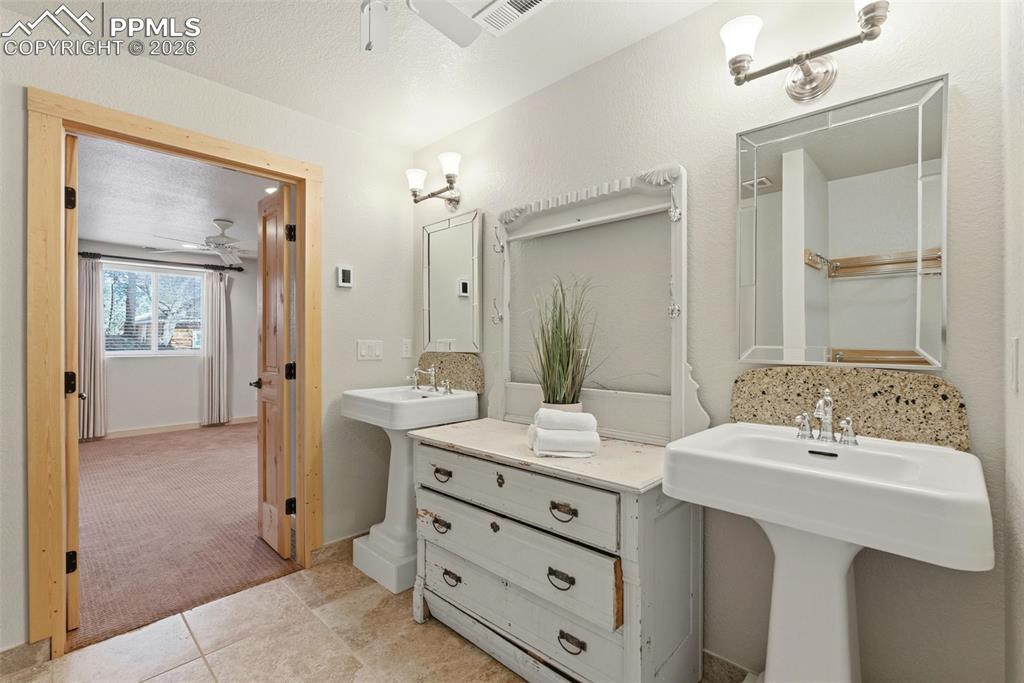 Full bathroom with ceiling fan, two sinks, light colored carpet, light tile patterned floors, and a textured ceiling