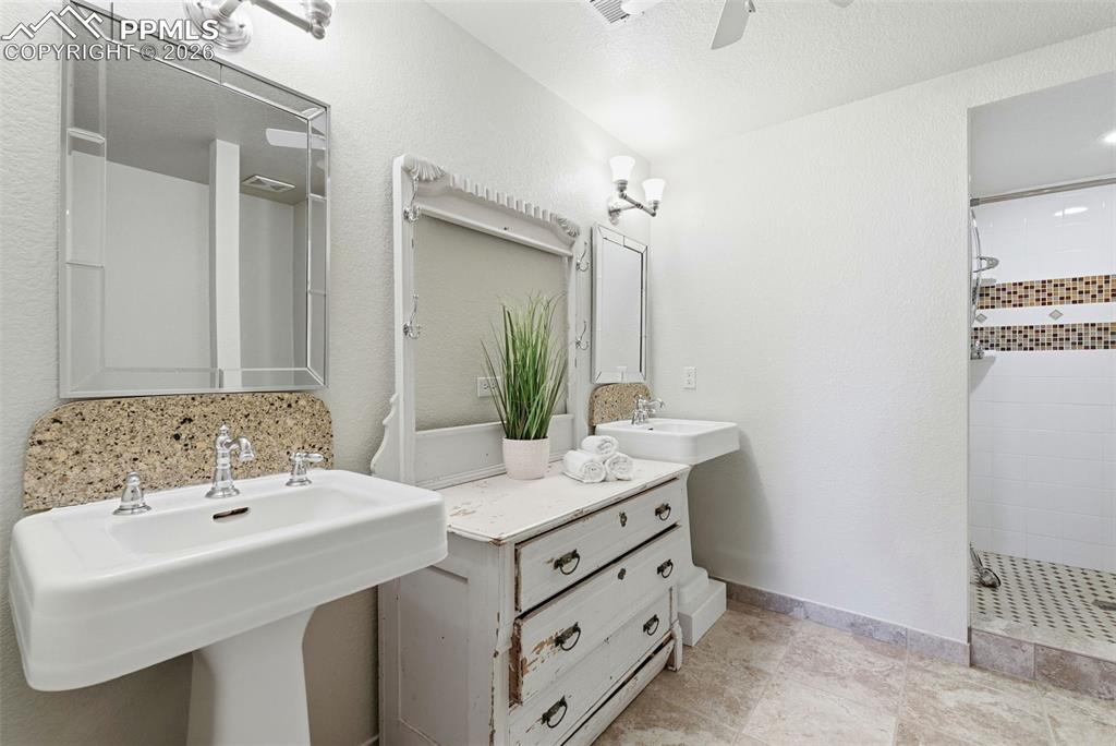 Full bath featuring two sinks, a shower stall, ceiling fan, a textured wall, and a textured ceiling