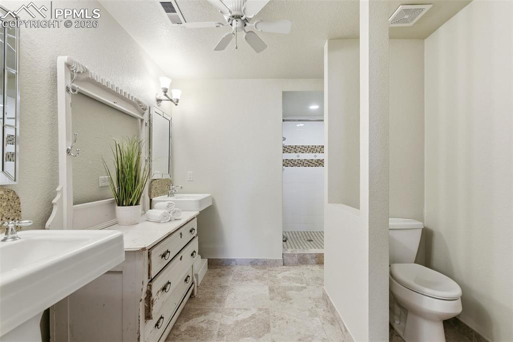 Full bathroom with walk in shower, a ceiling fan, a textured wall, a textured ceiling, and two vanities