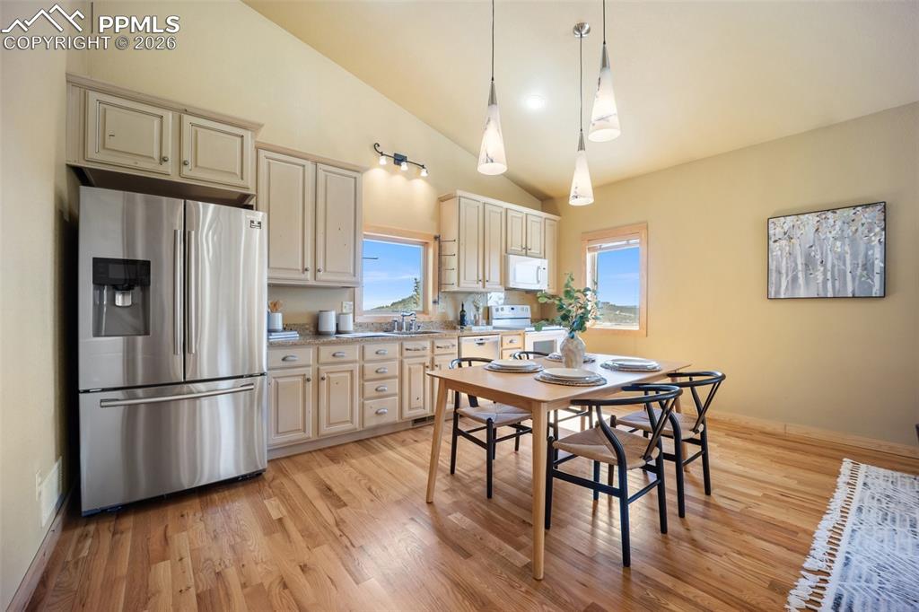 Kitchen with stainless steel appliances, vaulted ceiling, light wood-type flooring, hanging light fixtures, and cream cabinets