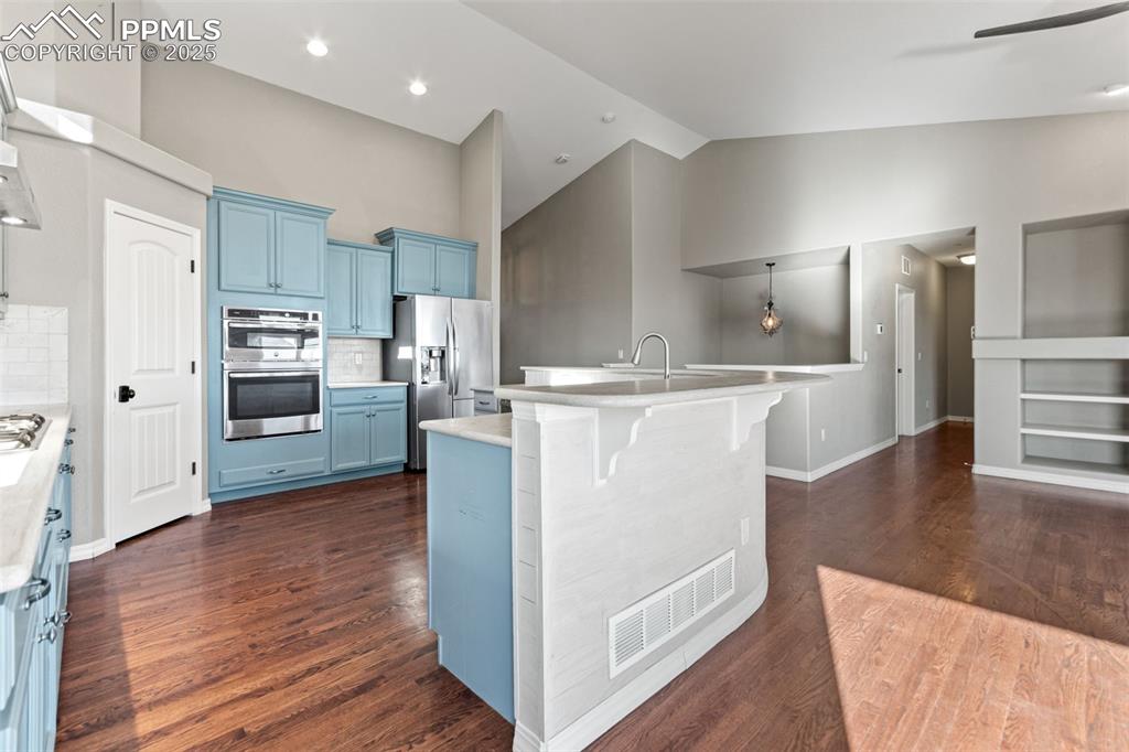 Kitchen featuring decorative backsplash, blue cabinets, appliances with stainless steel finishes, dark wood finished floors, and a kitchen breakfast bar