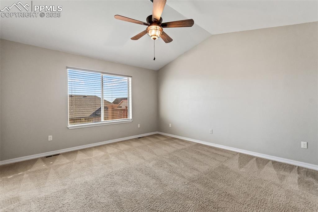 Spare room featuring vaulted ceiling, light carpet, and ceiling fan