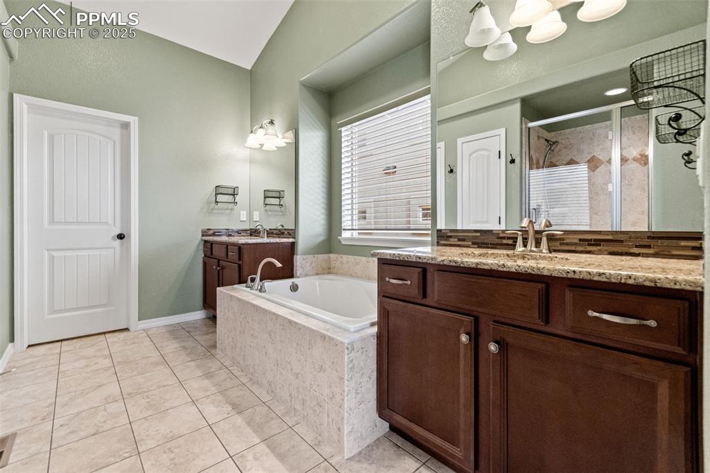 Bathroom with light tile patterned flooring, a bath, two vanities, a stall shower, and a chandelier