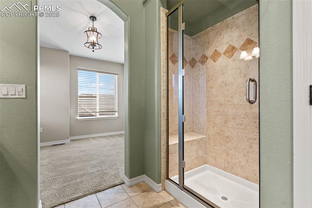 Bathroom featuring a chandelier, carpet, a shower stall, tile patterned flooring, and a textured wall