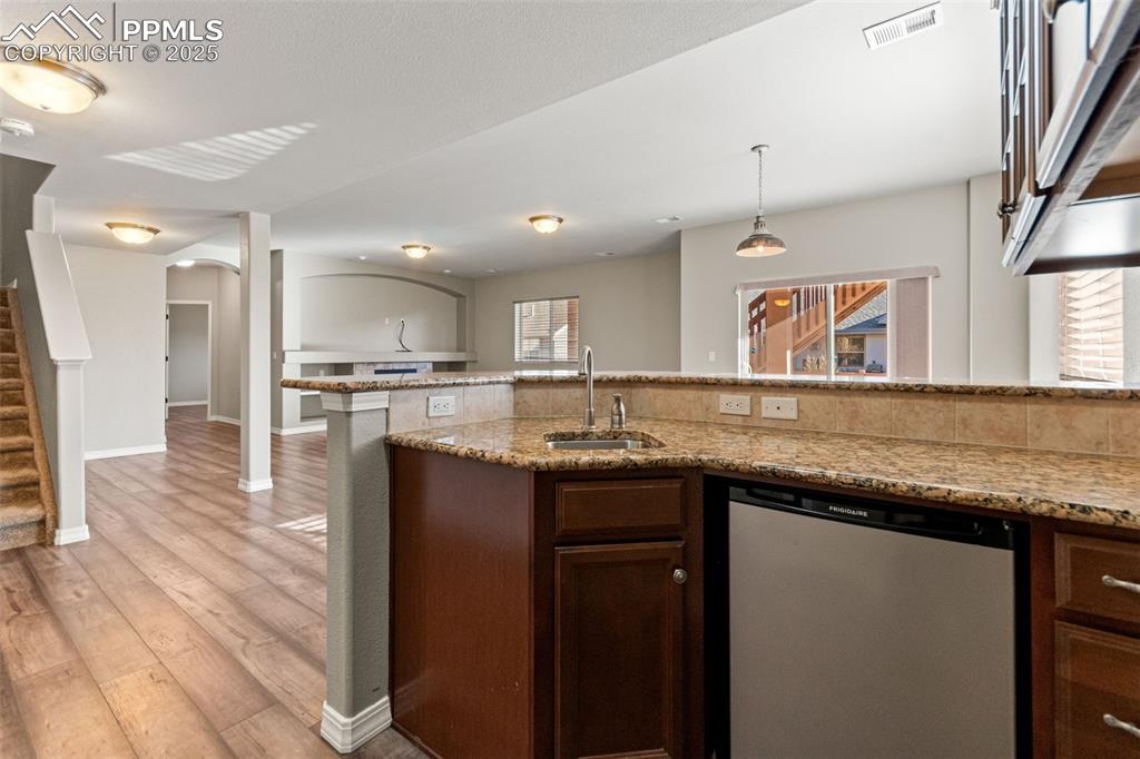 Kitchen with stainless steel dishwasher, light stone countertops, plenty of natural light, and light wood-style flooring