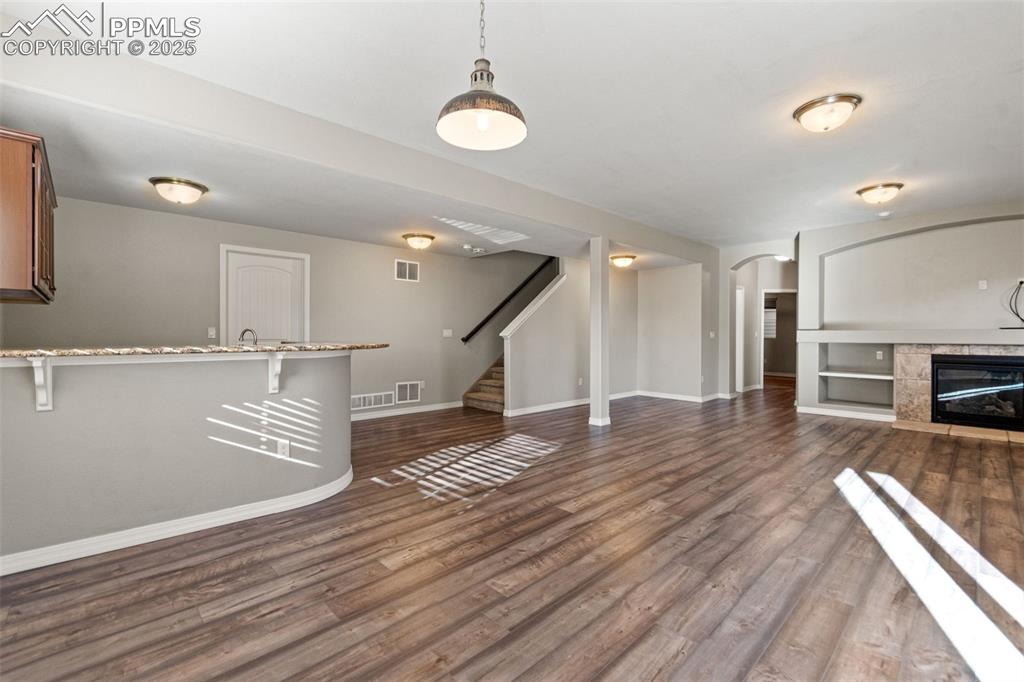 Unfurnished living room featuring dark wood-type flooring, a fireplace, stairs, and arched walkways