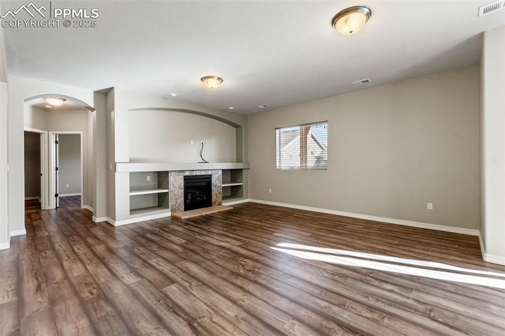 Unfurnished living room with arched walkways, a fireplace, and dark wood-type flooring