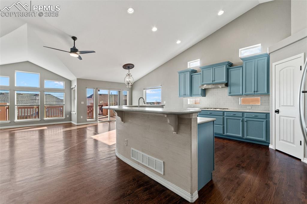 Kitchen with blue cabinetry, tasteful backsplash, high vaulted ceiling, a kitchen bar, and decorative light fixtures