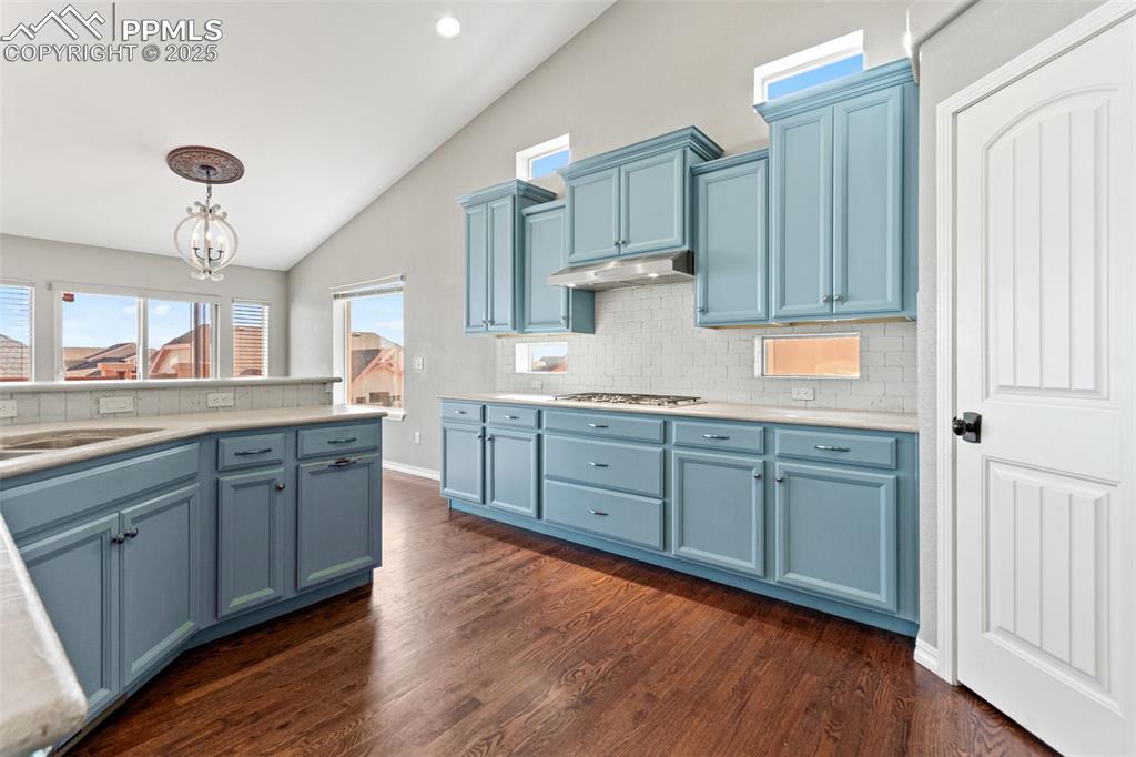Kitchen featuring backsplash, vaulted ceiling, blue cabinets, pendant lighting, and light countertops