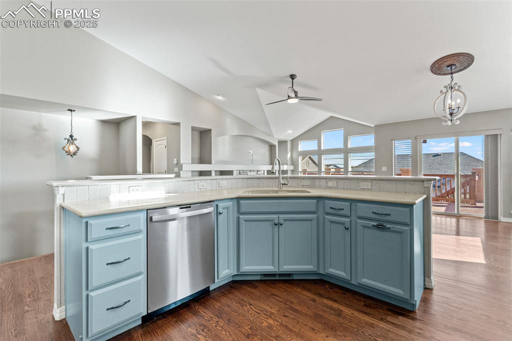 Kitchen with decorative light fixtures, vaulted ceiling, blue cabinetry, stainless steel dishwasher, and dark wood finished floors