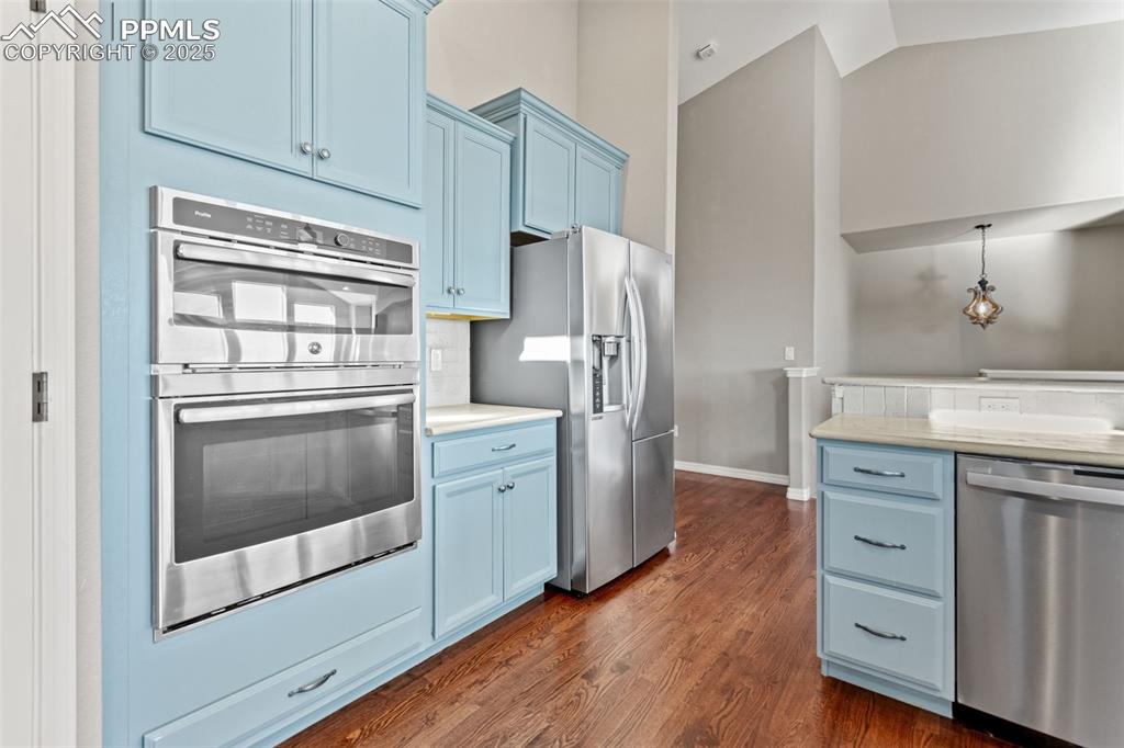 Kitchen featuring blue cabinets, stainless steel appliances, dark wood-style flooring, pendant lighting, and lofted ceiling