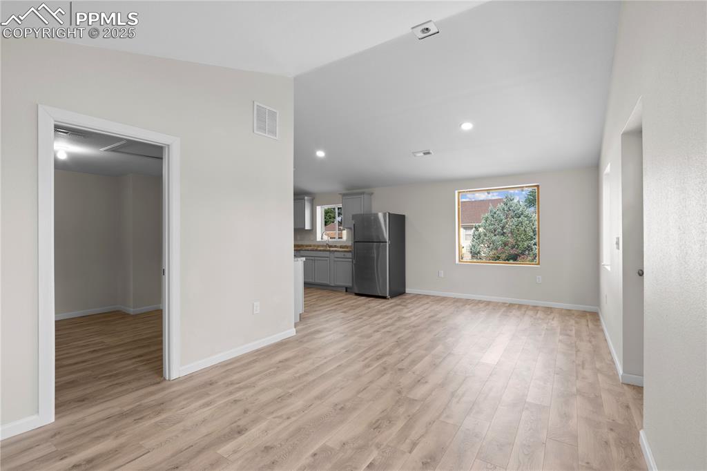 Unfurnished living room featuring light wood-type flooring and vaulted ceiling