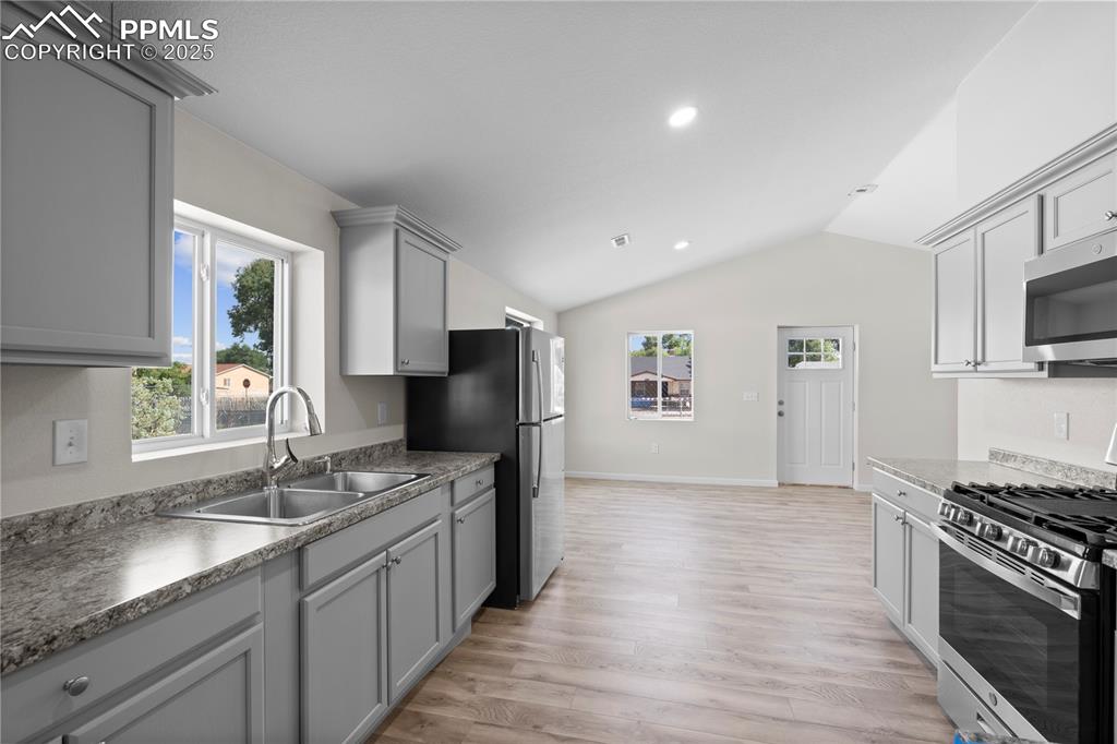 Kitchen with stainless steel appliances, gray cabinets, lofted ceiling, light wood-type flooring, and recessed lighting