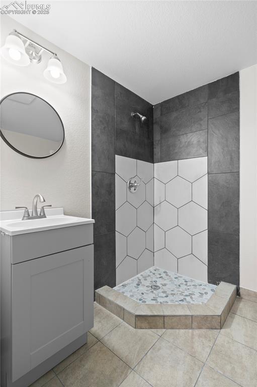 Full bath featuring tiled shower, vanity, and tile patterned flooring