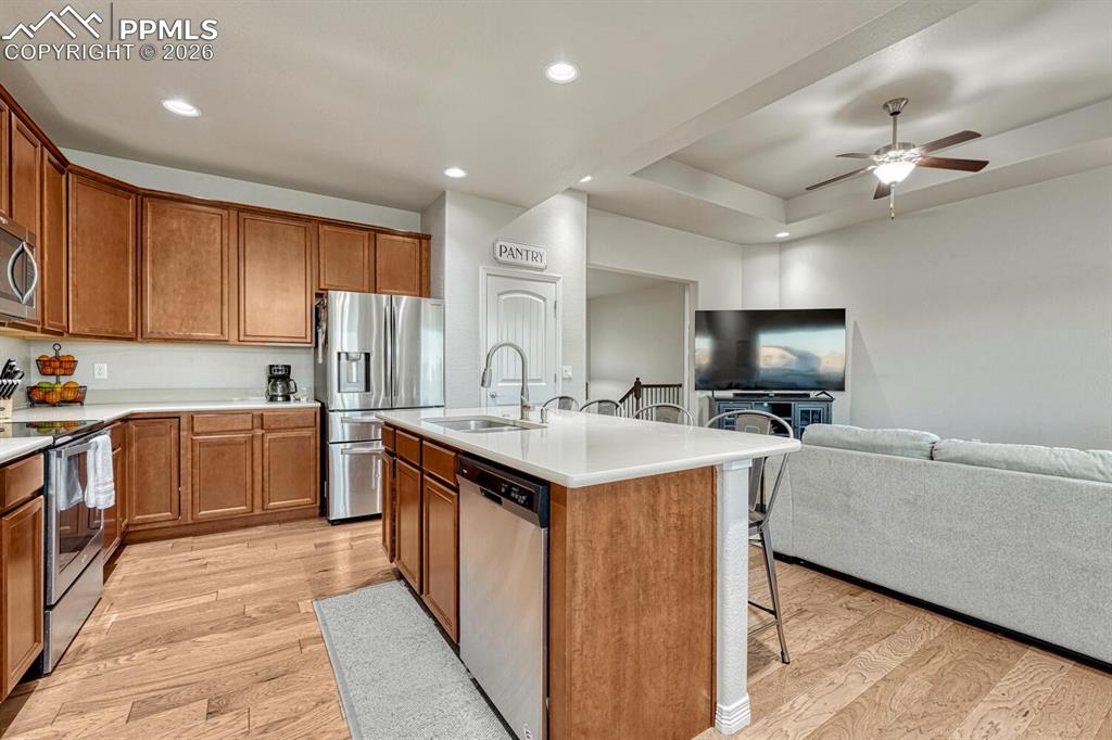 Kitchen featuring a breakfast bar, stainless steel appliances, brown cabinets, open floor plan, and light wood finished floors