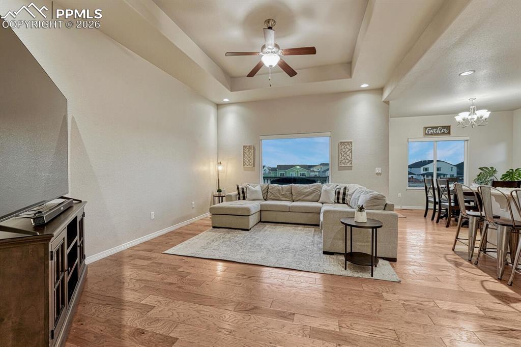 Living room with a tray ceiling, light wood-style flooring, a chandelier, ceiling fan, and recessed lighting