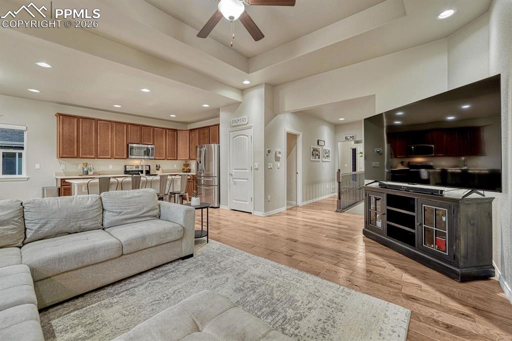 Living area featuring a ceiling fan, light wood-style floors, recessed lighting, and a raised ceiling