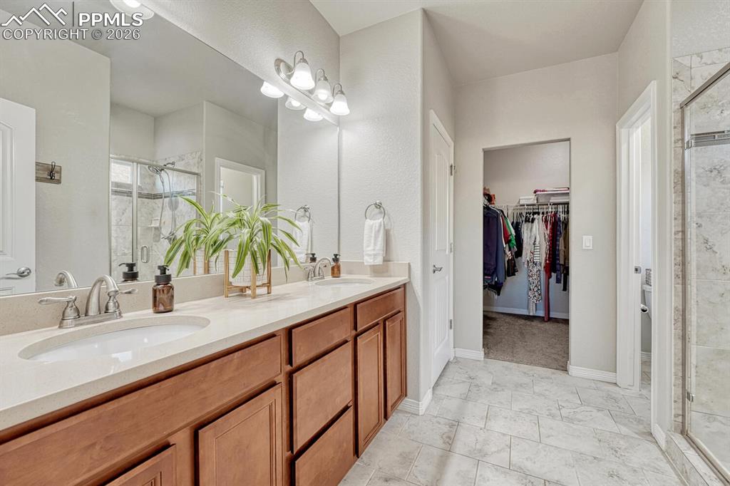 Full bath with a shower stall, double vanity, and a walk in closet