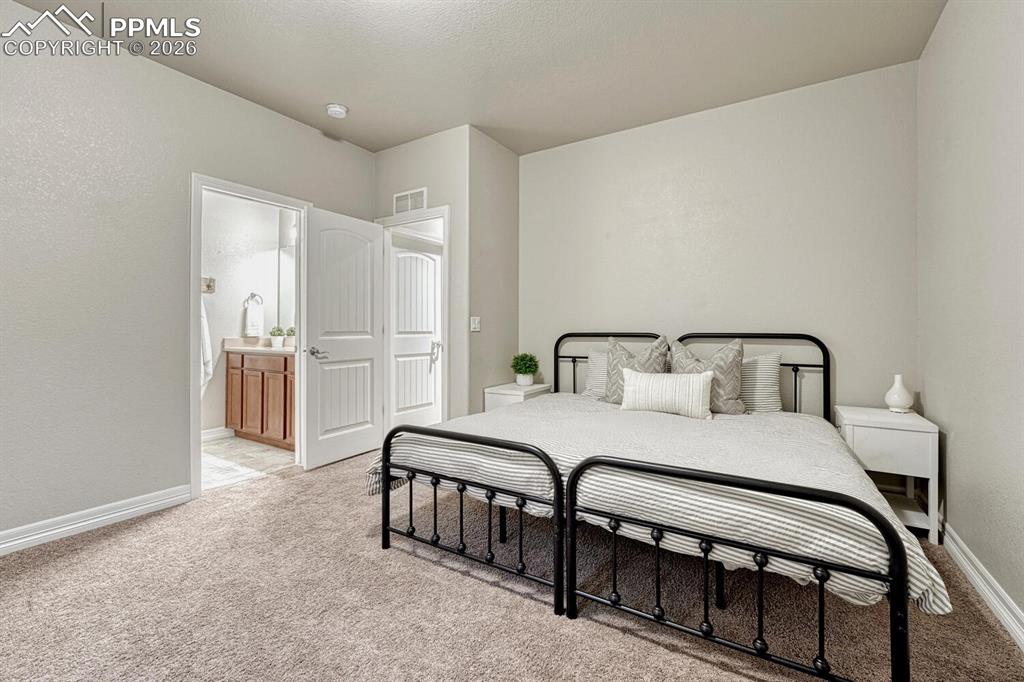Bedroom with light carpet, a textured wall, and ensuite bathroom