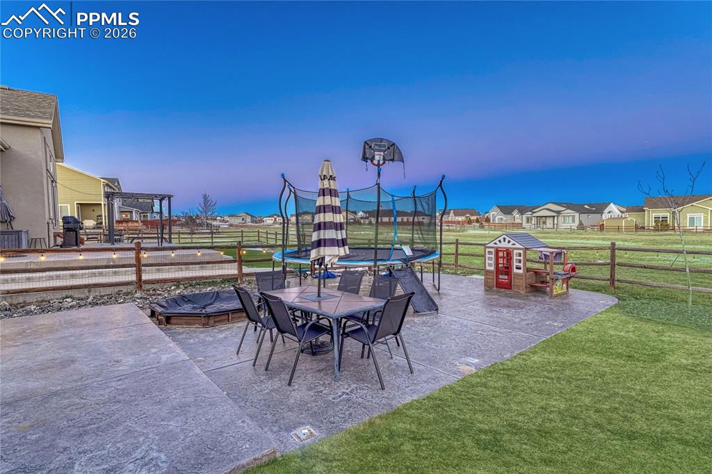 Fenced backyard with a trampoline, outdoor dining space, a patio, a residential view, and a grill