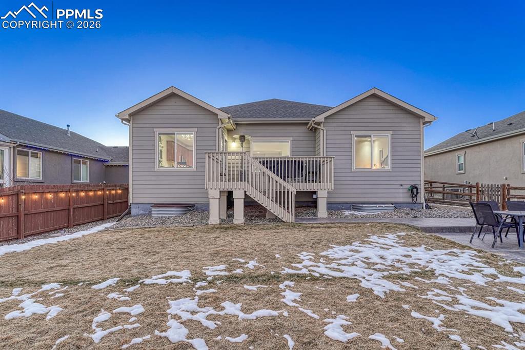 Snow covered back of property featuring a fenced backyard, a wooden deck, roof with shingles, and a patio area