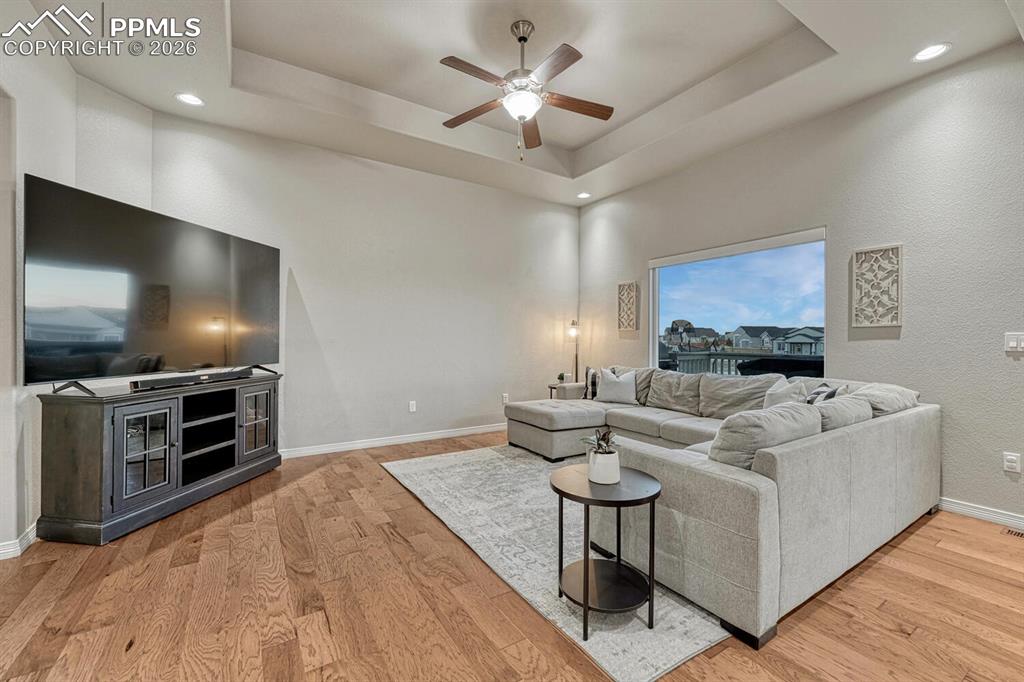 Living room featuring recessed lighting, light wood-type flooring, a ceiling fan, and a tray ceiling