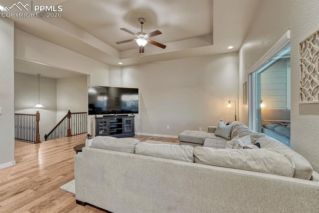 Living room featuring recessed lighting, light wood finished floors, a tray ceiling, a ceiling fan, and a towering ceiling