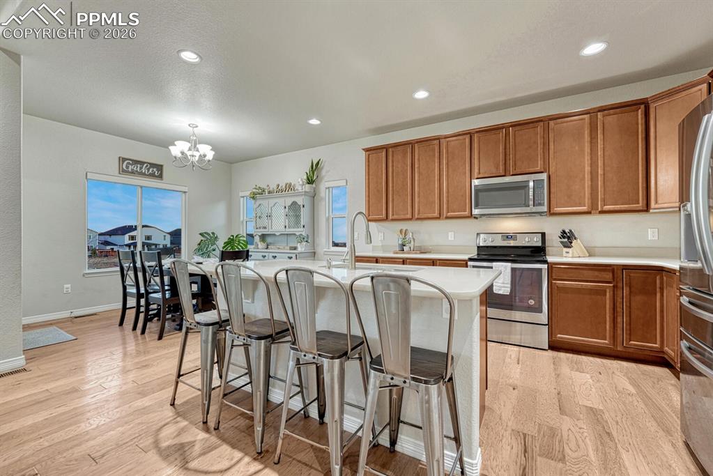 Kitchen featuring appliances with stainless steel finishes, brown cabinetry, a breakfast bar area, recessed lighting, and pendant lighting