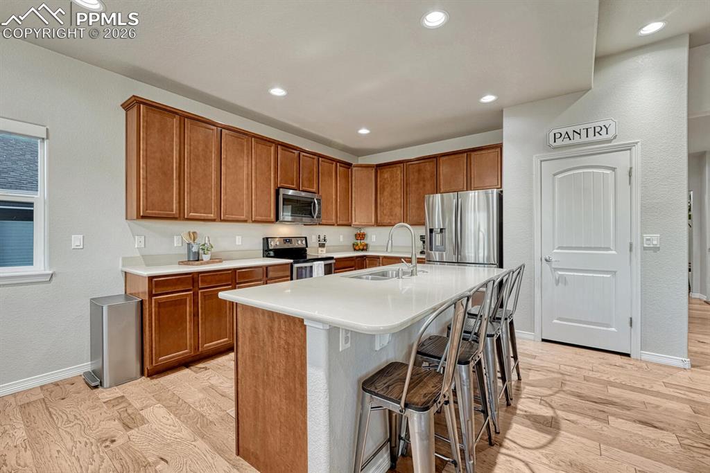 Kitchen featuring light wood-style floors, brown cabinets, a kitchen bar, appliances with stainless steel finishes, and recessed lighting
