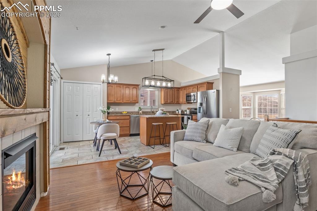 Living area featuring a chandelier, a fireplace, ceiling fan, lofted ceiling, and light wood-style flooring